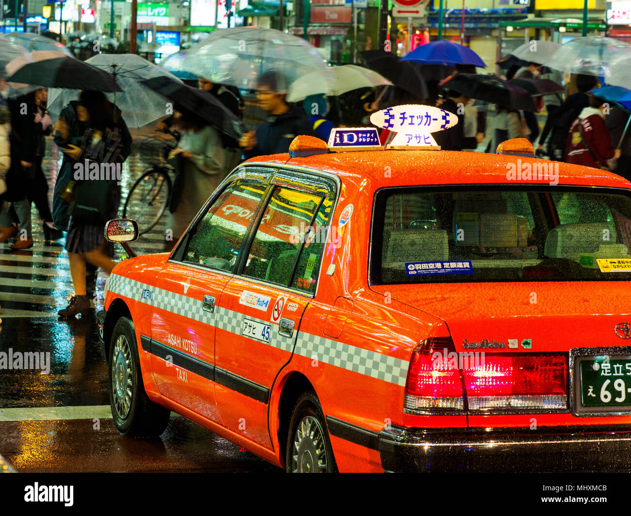 Vibrant Tokyo Nightlife - colourful taxi waits as people cross the road on a rainy night Stock Photo