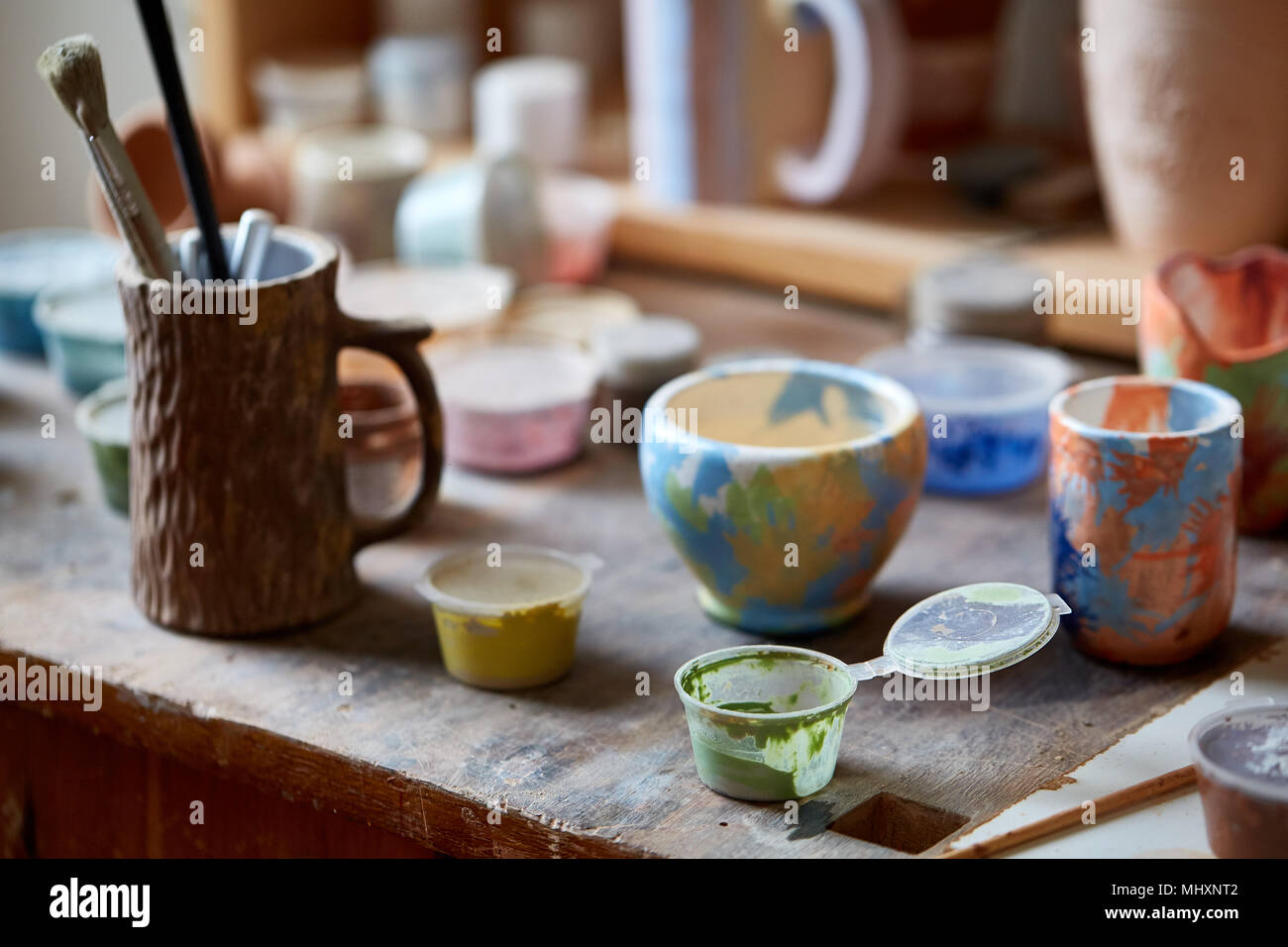 Close Up Of Various Paint Mugs And Brushes In Holder On Worktop