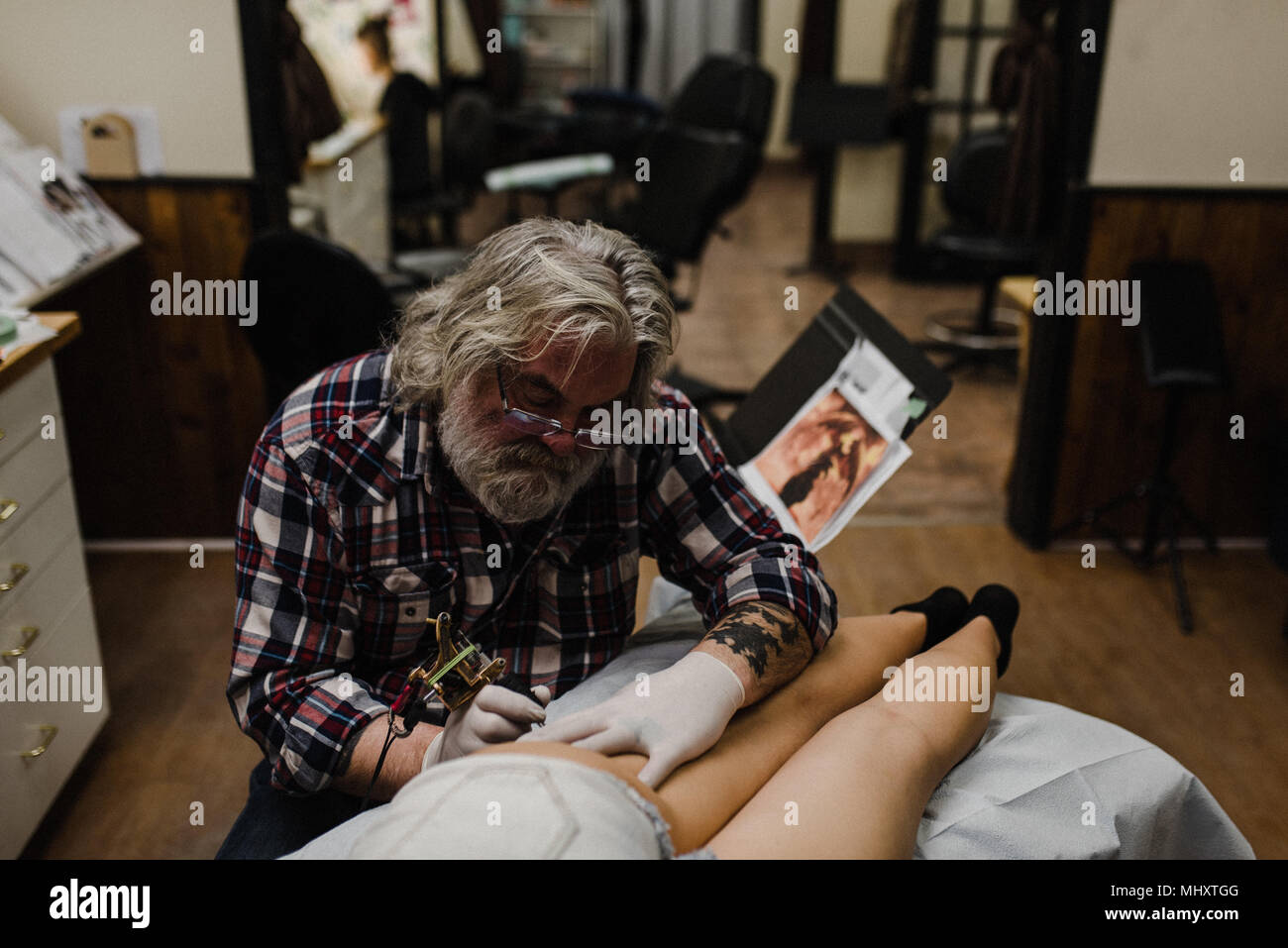 Tattooist tattooing young woman's thigh Stock Photo