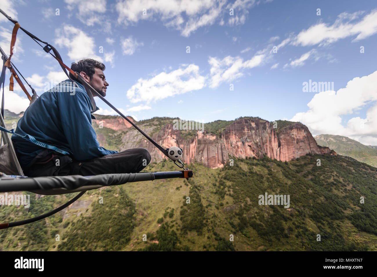 Rock climber sitting on portaledge, looking at view, Liming, Yunnan Province, China Stock Photo