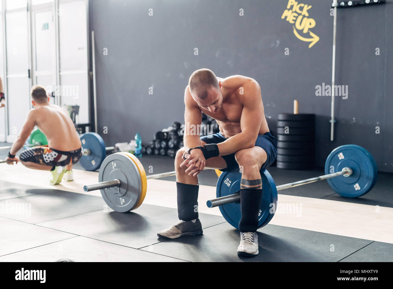 Exhausted man in gym sitting on barbell Stock Photo