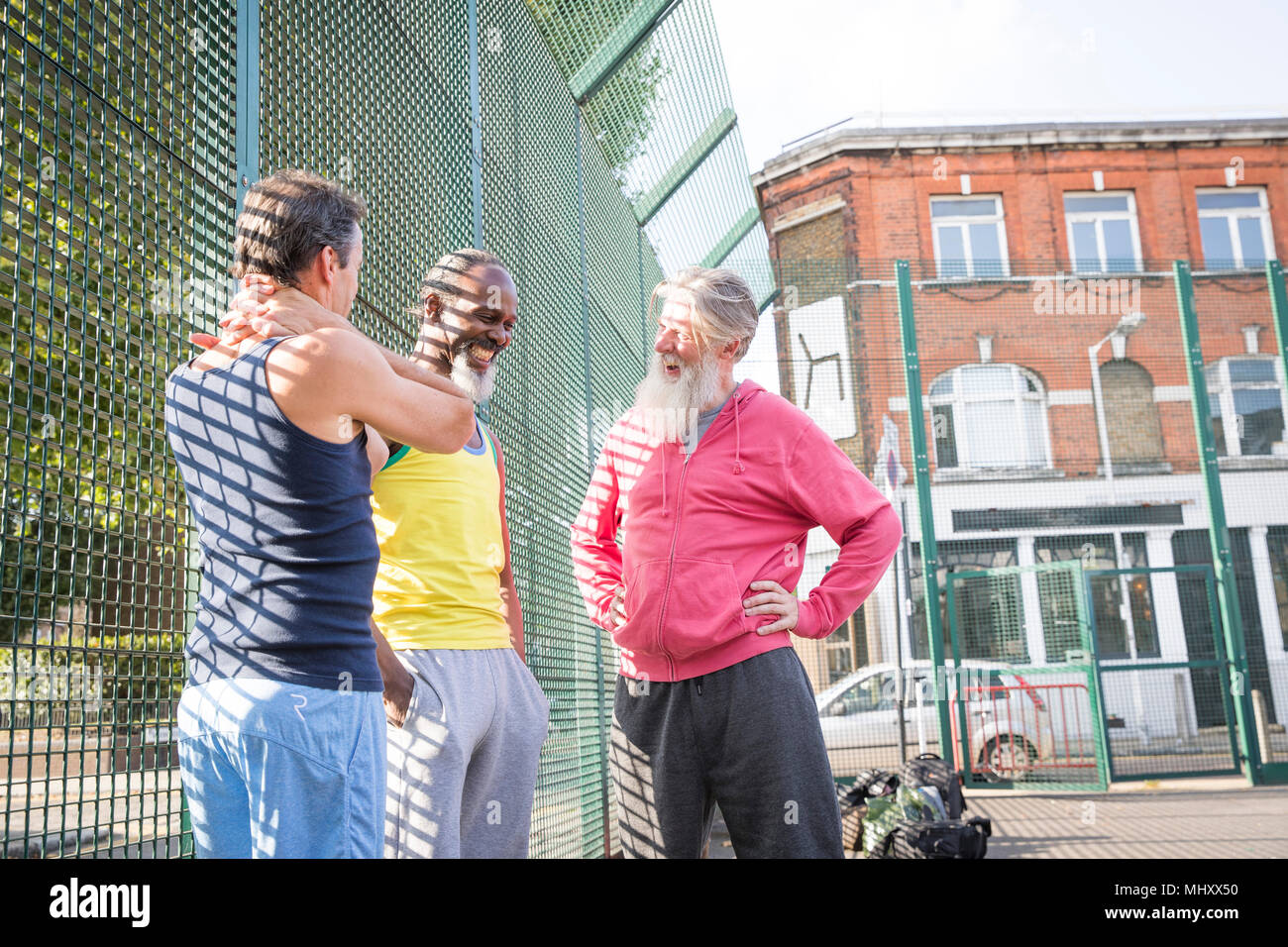 Three mature men in basketball court, laughing together Stock Photo