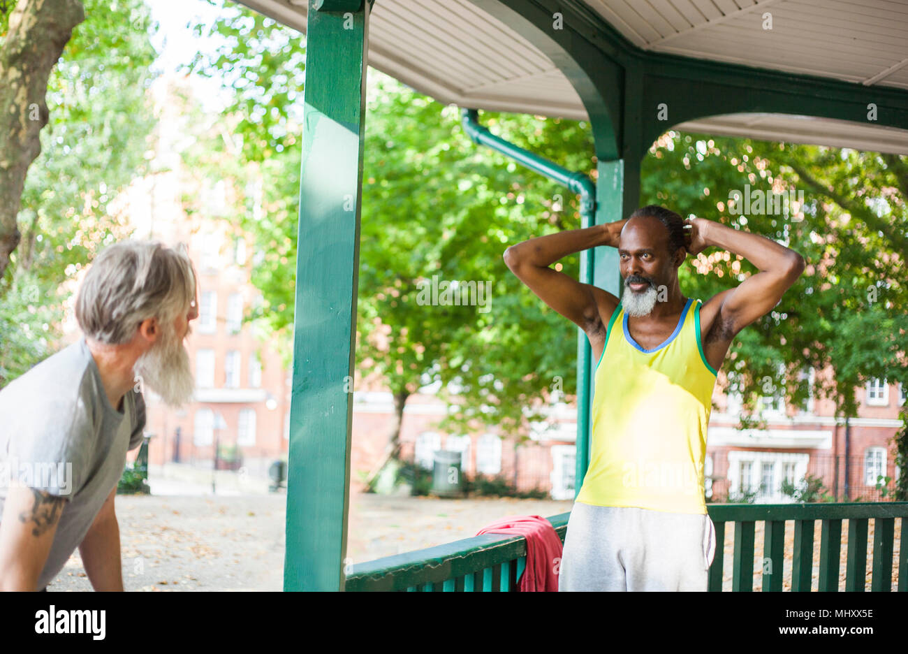 Two mature men standing under bandstand, taking a break from exercise Stock Photo