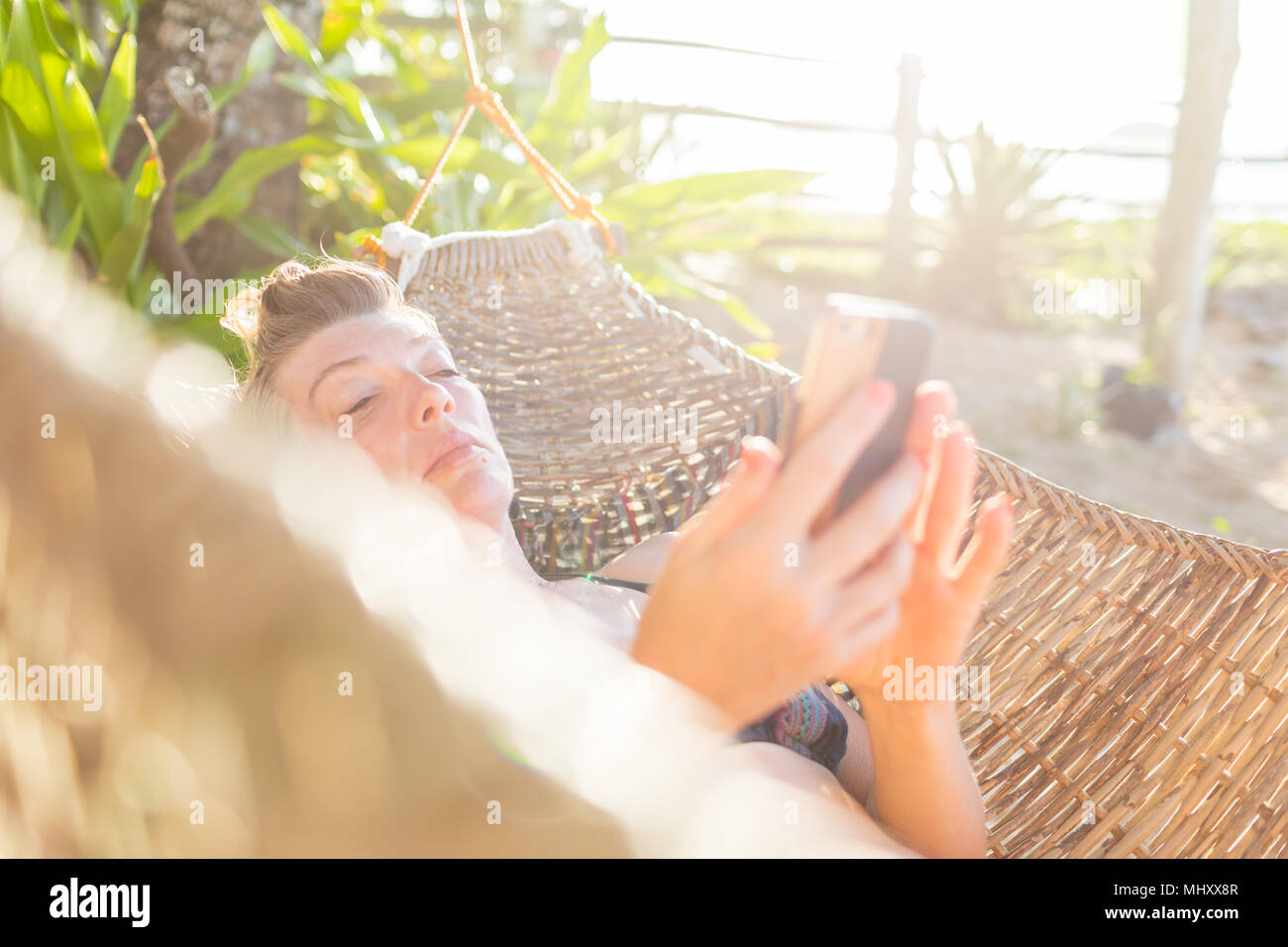 Woman relaxing on hammock, using smartphone,  Nacpan Beach, Palawan, Philippines Stock Photo