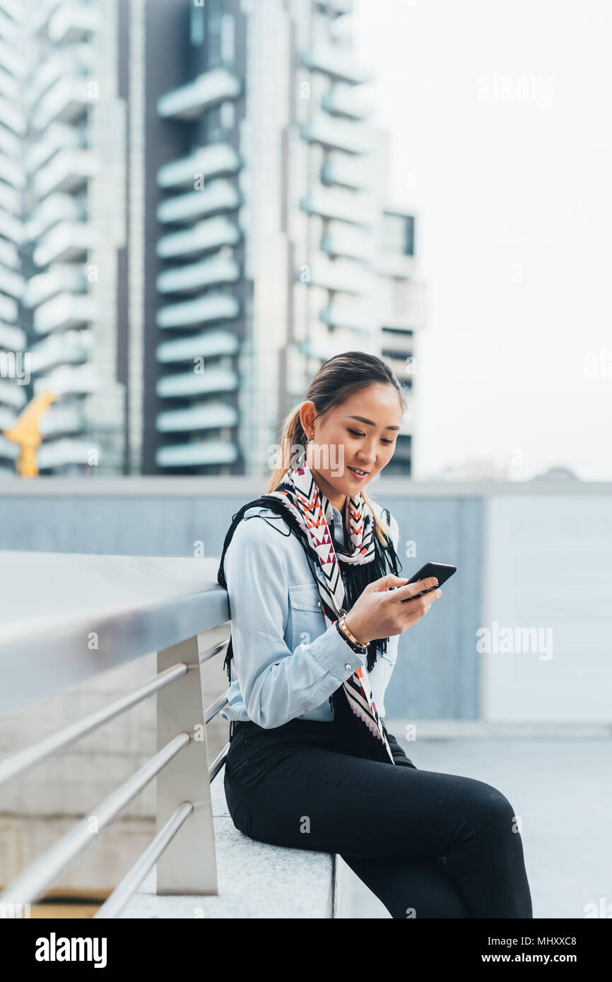 Businesswoman sitting outdoors, using smartphone Stock Photo