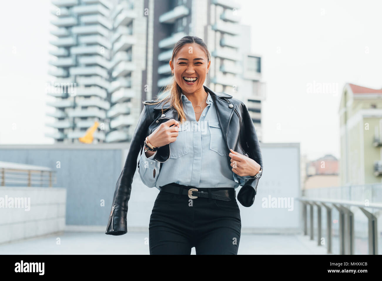 Portrait of businesswoman outdoors, wearing leather jacket around shoulders, laughing Stock Photo