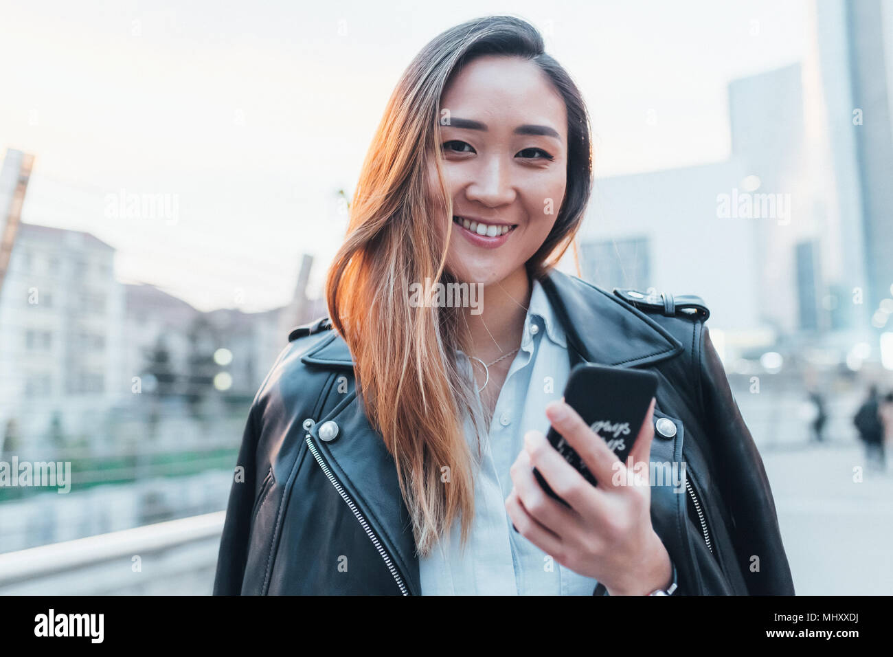 Portrait of businesswoman outdoors, holding smartphone, smiling Stock Photo