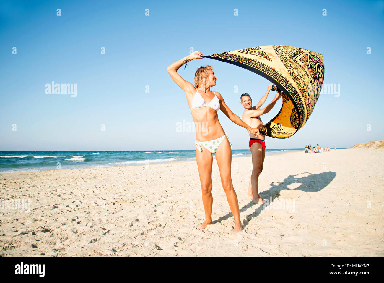 Mature couple on beach, holding beach blanket, laughing Stock Photo
