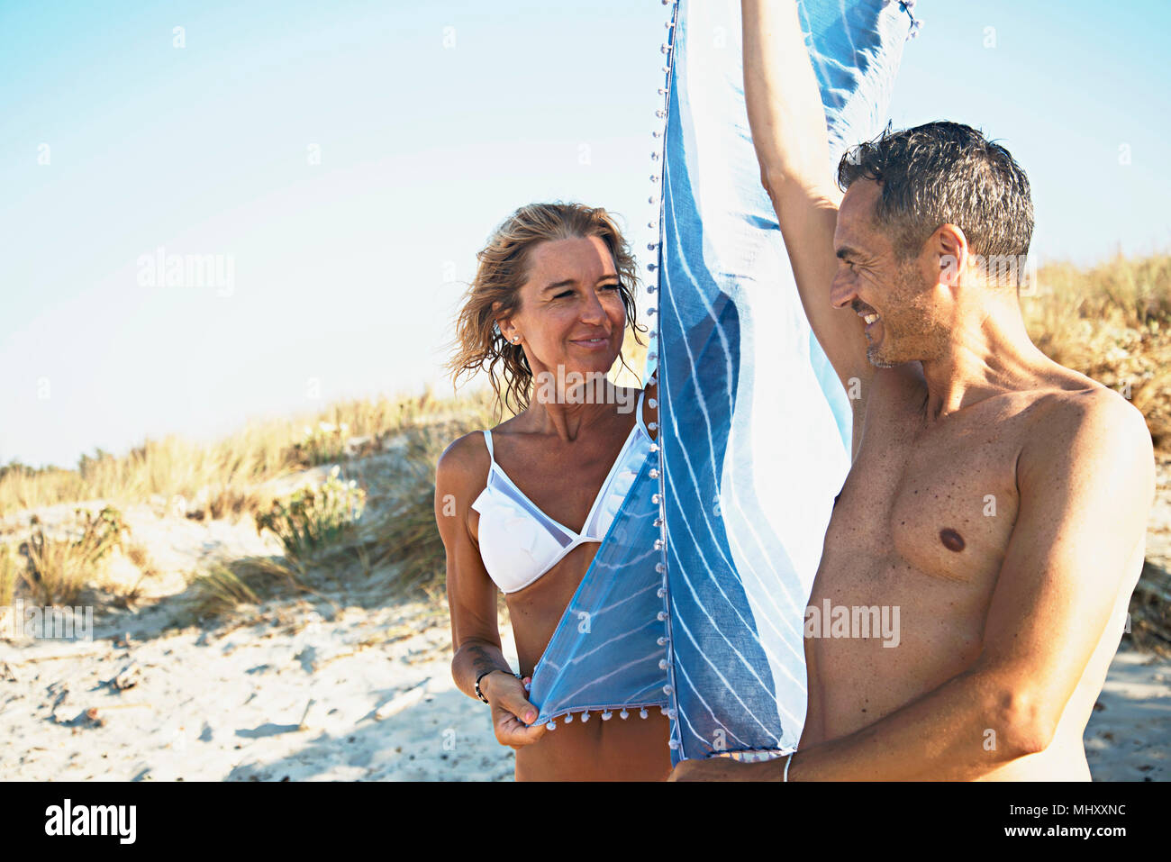 Mature couple on beach, holding beach blanket between them, smiling Stock Photo