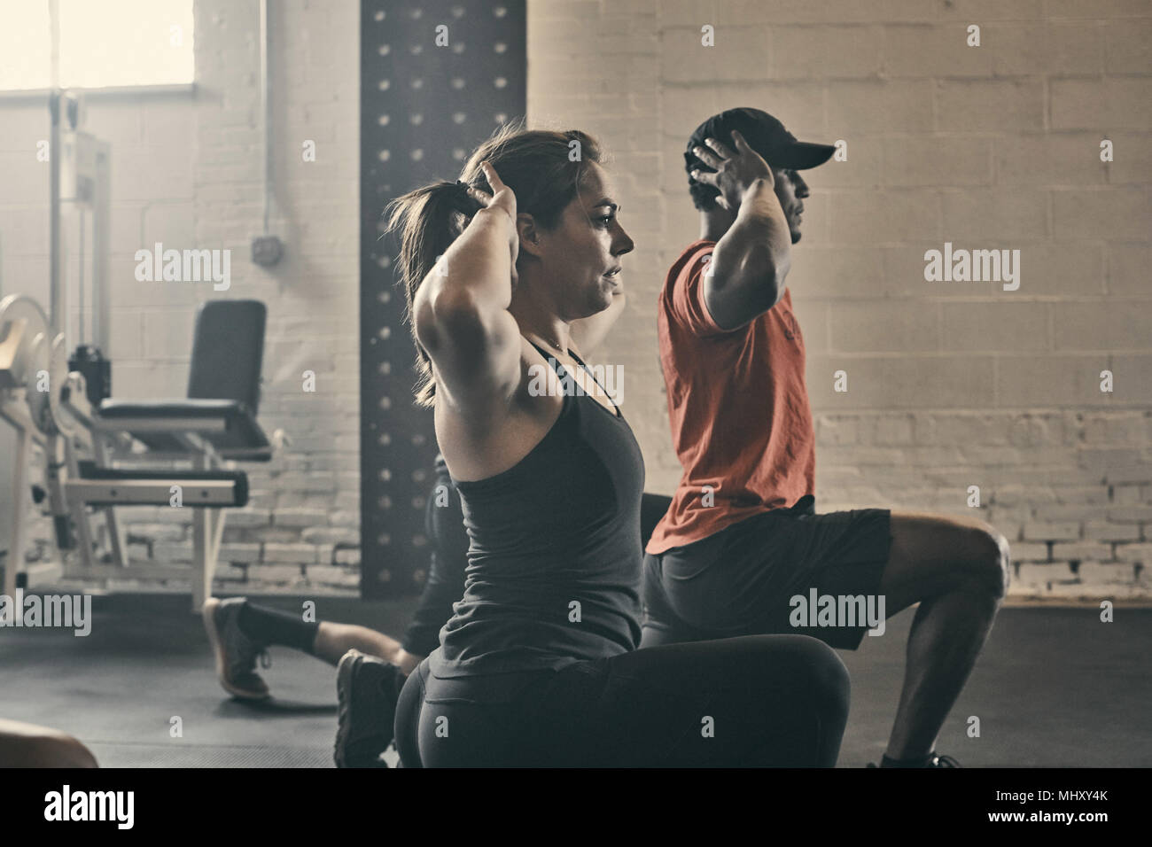 People exercising in gym, hands behind head lunging Stock Photo