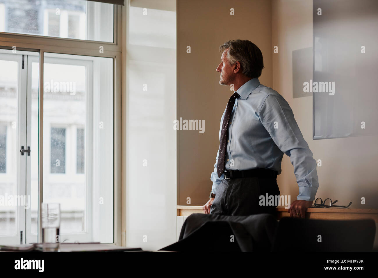 Businessman in office looking out of window pensively Stock Photo