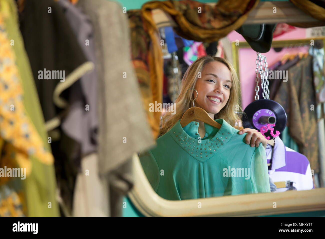 Mirror image of young woman trying on vintage clothes in thrift store Stock Photo