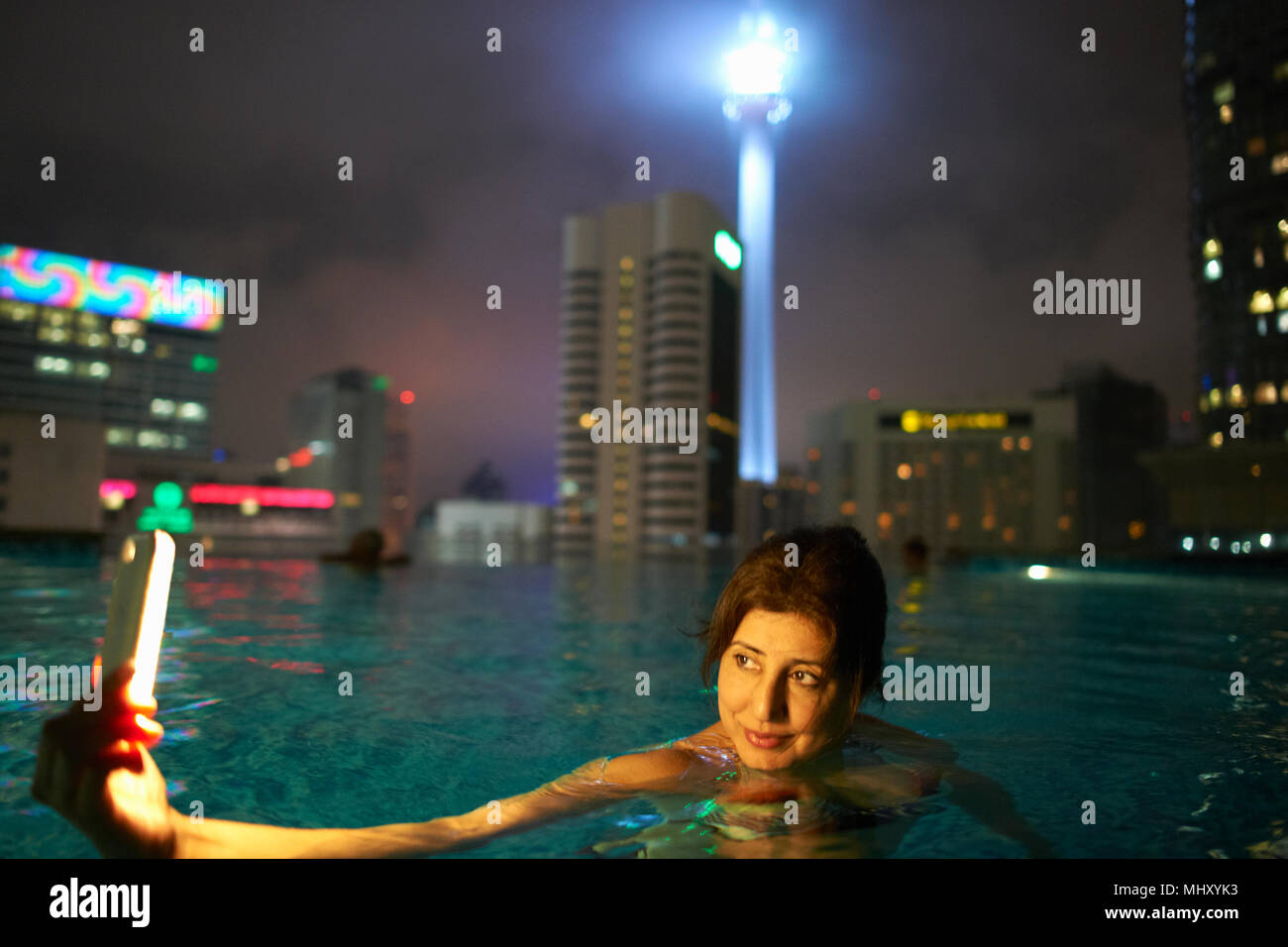 Tourist taking selfie in rooftop pool, KL Tower in background, Kuala Lumpur, Malaysia Stock Photo