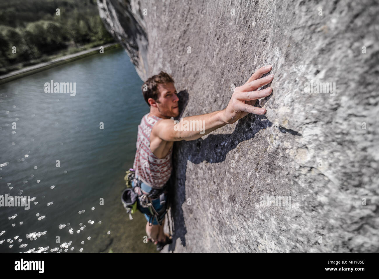 Young male rock climber reaching while climbing limestone rock face, Freyr, Belgium, elevated view Stock Photo
