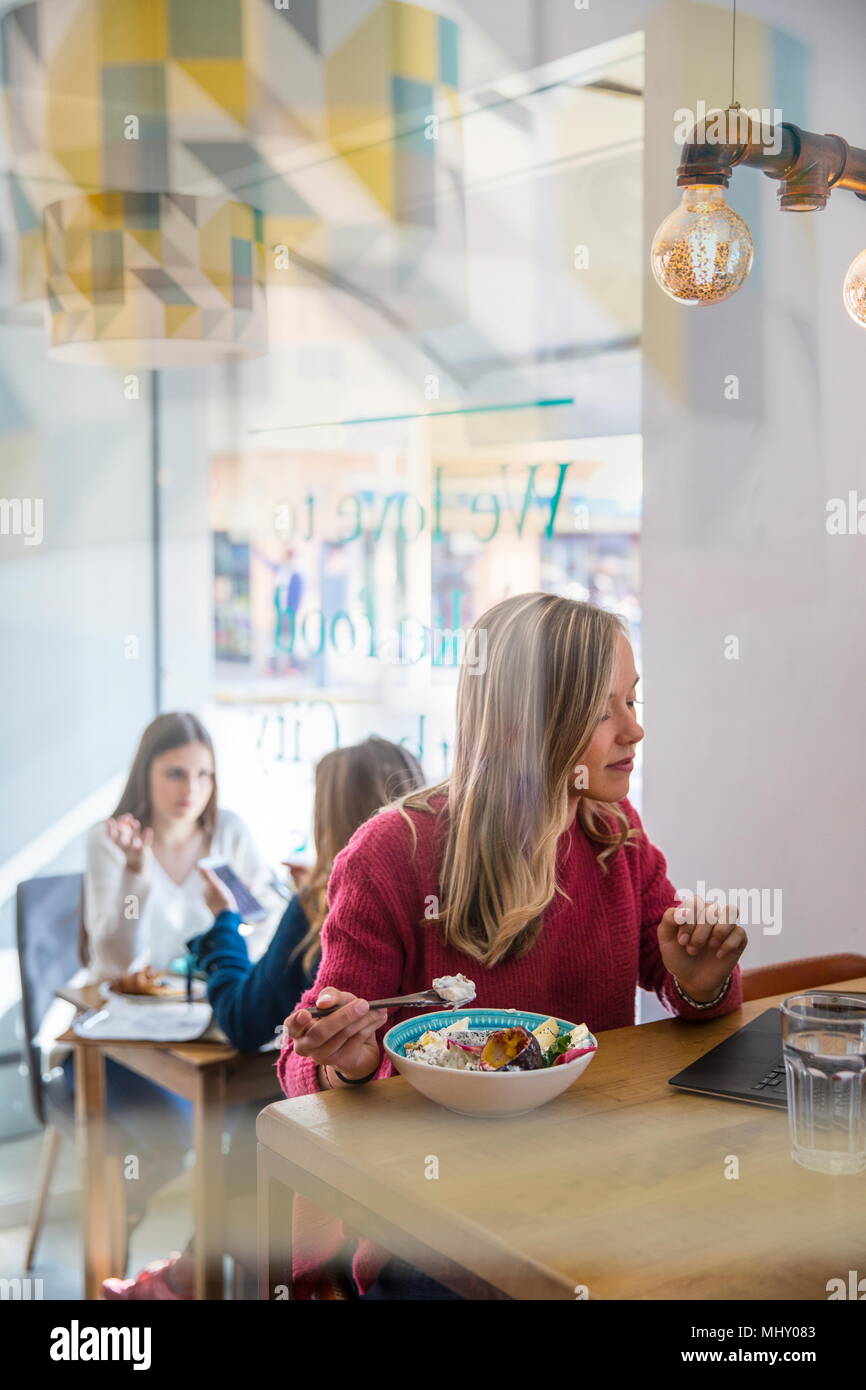 Woman eating muesli in cafe, using laptop Stock Photo