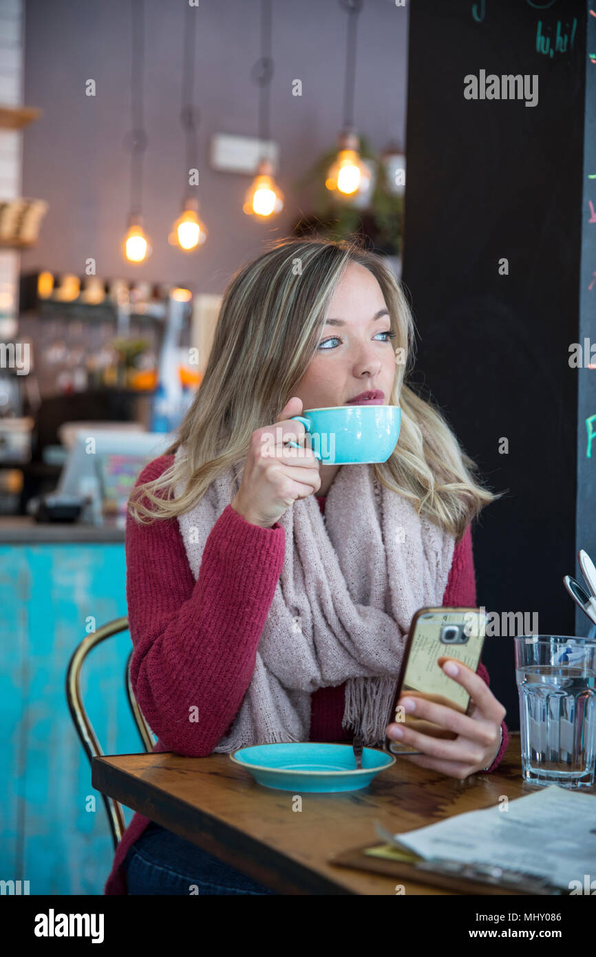 Woman sitting in cafe, holding smartphone, drinking coffee Stock Photo