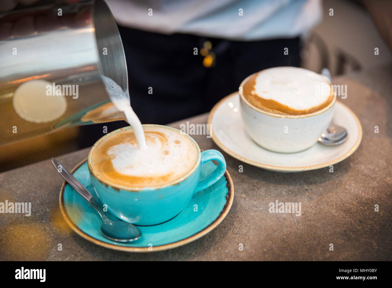 Barista pouring frothy milk into coffee cup, close-up Stock Photo