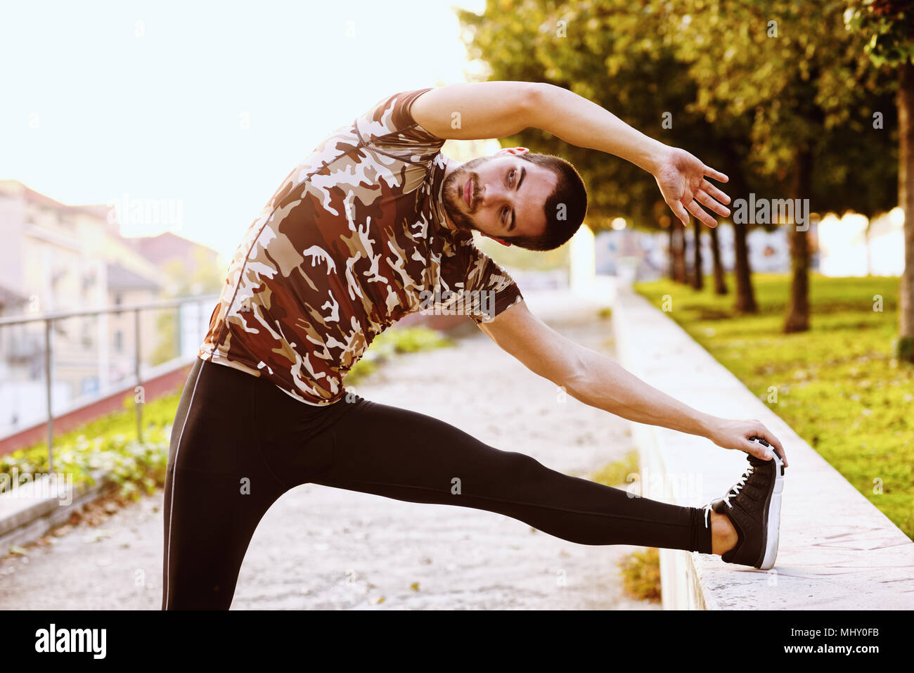 Young man exercising outdoors, stretching with foot on wall Stock Photo