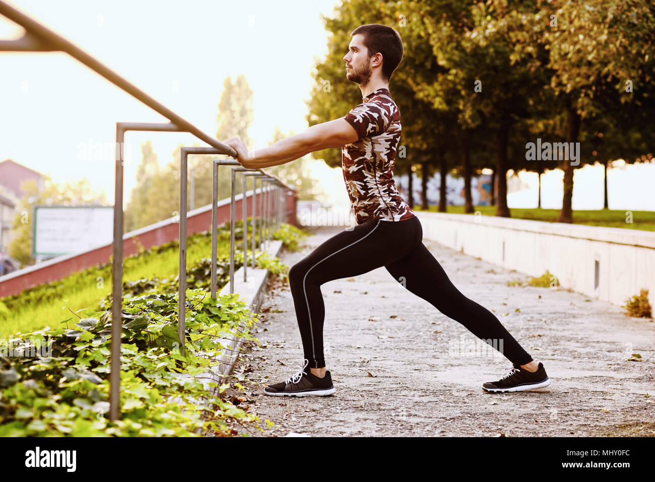 Young man exercising outdoors, stretching, holding onto railings Stock Photo