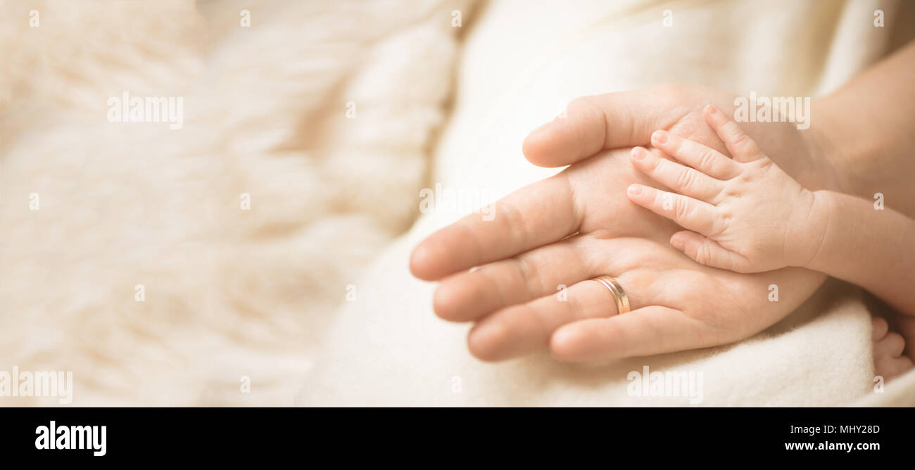 Female hand holding her newborn baby's hand. Mom with her child. Maternity, family, birth concept. Copy space for your text. Banner Stock Photo