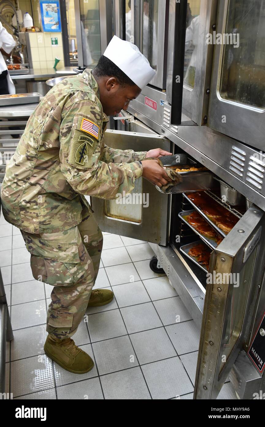 U.S. Army Spc, May 3, 2018. Hubert Ramsey, a culinary specialist with Fury Battery, 4th Battalion, 319th Airborne Field Artillery Regiment, 173rd Airborne Brigade, pulls a pan from an oven at the Tower Barracks Dining Facility, Grafenwoehr, Germany, May 3, 2018. (U.S. Army photo by Gertrud Zach). () Stock Photo
