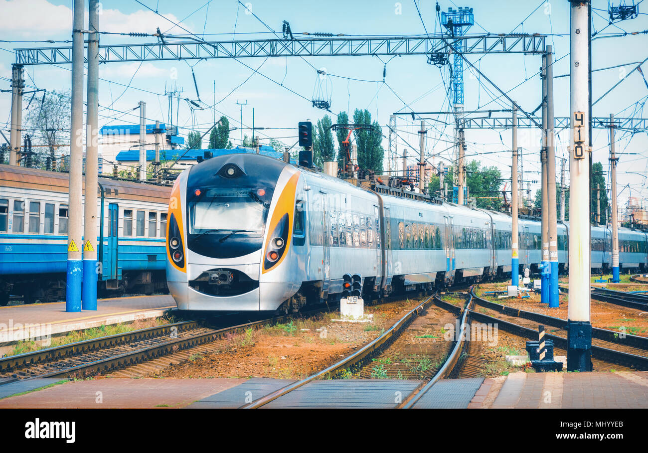 High speed train arrives on the railway station at sunset in Europe. Modern intercity train on the railway platform. Industrial landscape with passeng Stock Photo