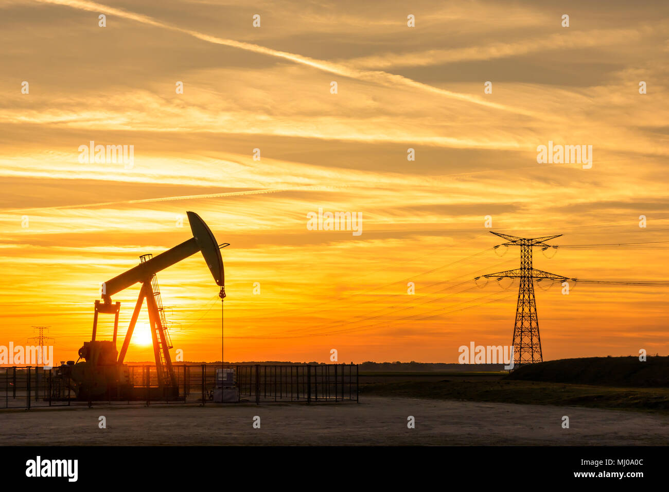 Pumpjack and transmission towers at sunset symbolizing ecological transition. A pump jack with electricity pylons and power line against a red sky. Stock Photo