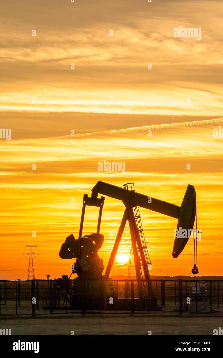 Pumpjack and transmission towers at sunset symbolizing ecological transition. A pump jack with electricity pylons and power line against a red sky. Stock Photo