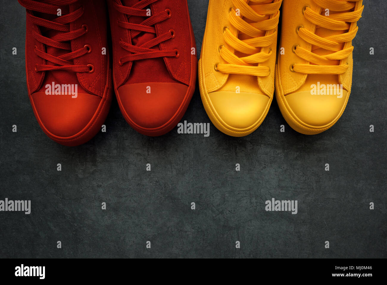 Young adult people on a love date, conceptual image. Top view of two pair of casual sneakers, yellow and red, from above close next to each other like Stock Photo