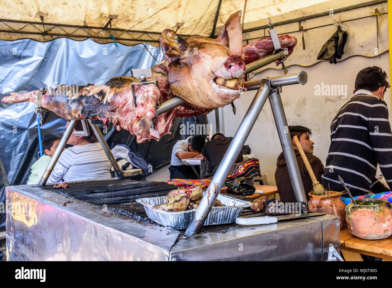 Santiago Sacatepequez, Guatemala - November 1, 2017: Whole roasted pig on spit at streetside food stall during giant kite festival on All Saints' Day Stock Photo