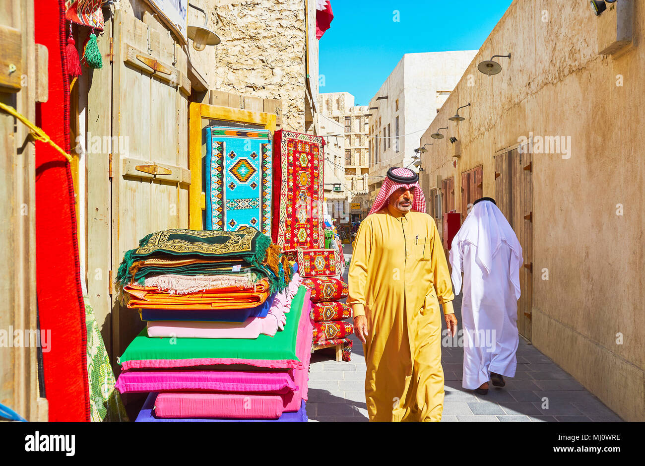 DOHA, QATAR - FEBRUARY 13, 2018:  Qatari men walk along the street of Souq Waqif in traditional attire - keffiyeh (headscarf) and dishdasha or thobe ( Stock Photo