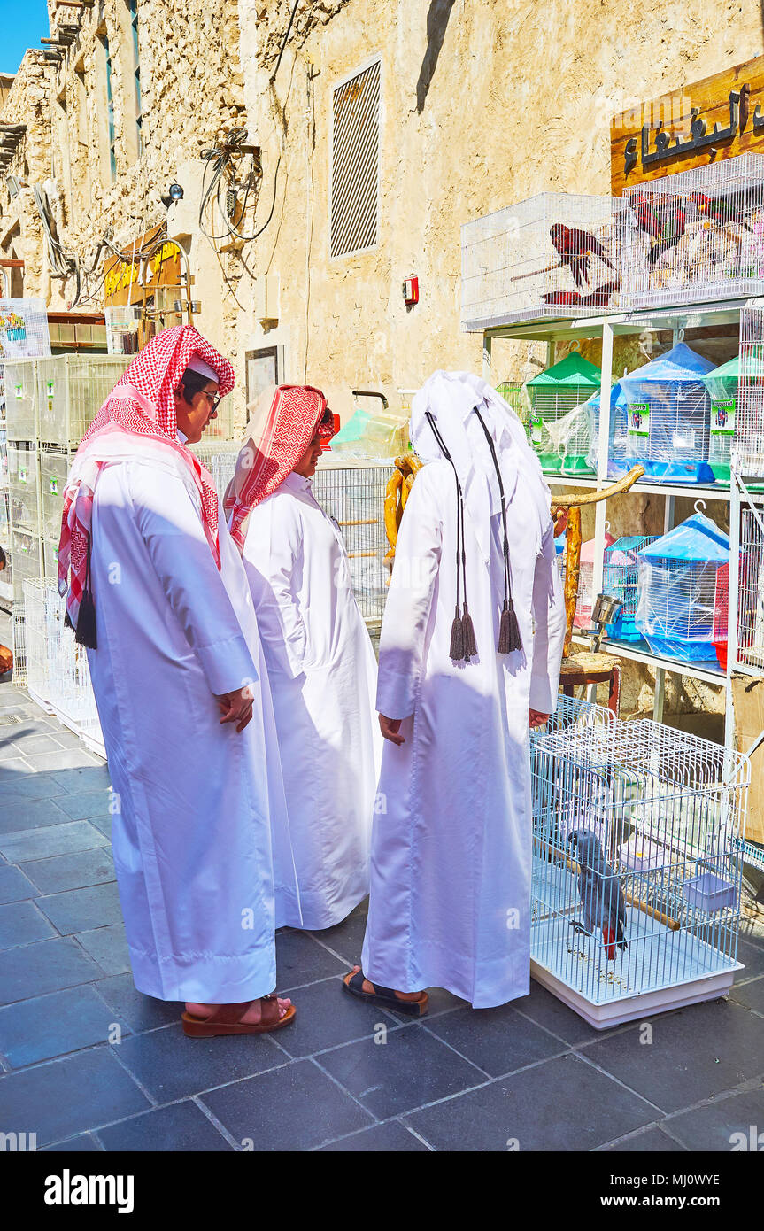 DOHA, QATAR - FEBRUARY 13, 2018: Qatari teens, dressed in traditional attire (keffiyeh and thobe), choose the pet birds at the store of Birds market i Stock Photo