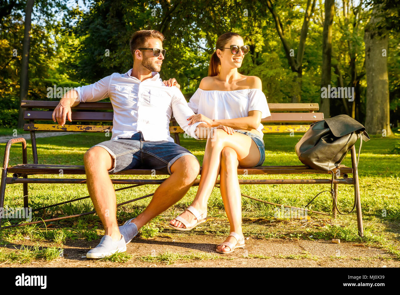 A beautiful young couple sitting on a bench in a park in the sunset Stock  Photo - Alamy