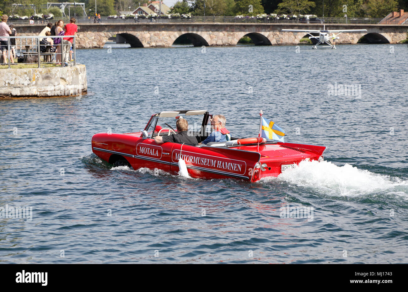 Motala, Sweden - August 8, 2015: Red amphibious Amphicar associated with the Motala Motor Museum running in the water with two people on board. Stock Photo