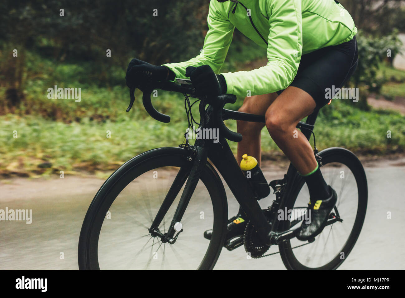 Professional cyclist riding bike outdoors. Male athlete in cycling gear practising on wet road. Cropped shot. Stock Photo