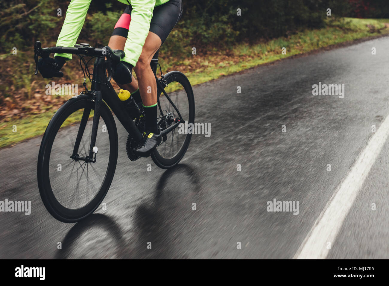 Male athlete in cycling gear riding bike on wet road. Low section shot of cyclist training outdoors on a rainy day. Stock Photo