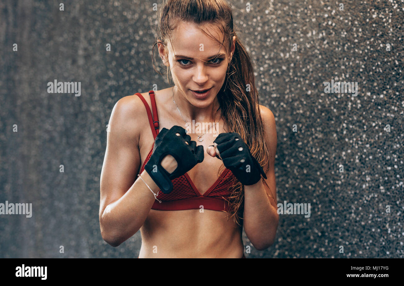 Female wearing gloves ready to fight. Woman boxer exercising outdoors against grey wall. Stock Photo