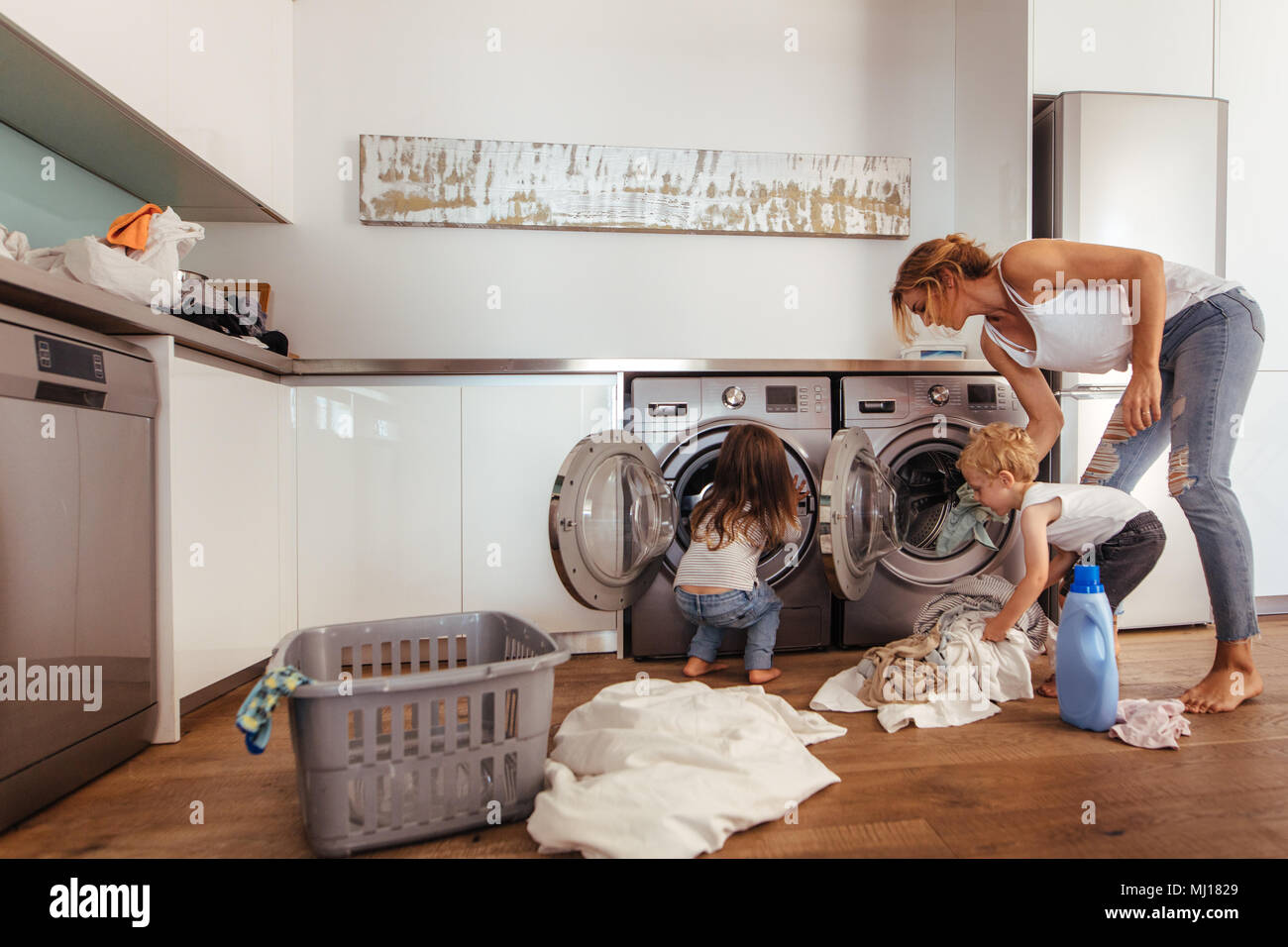 Woman with kids load clothes in washing machine. Mother and children putting laundry into washing machine at home. Stock Photo