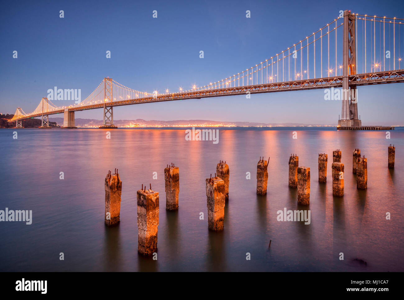The San Francisco Bay Bridge at night and old concrete jetty pilings. Stock Photo