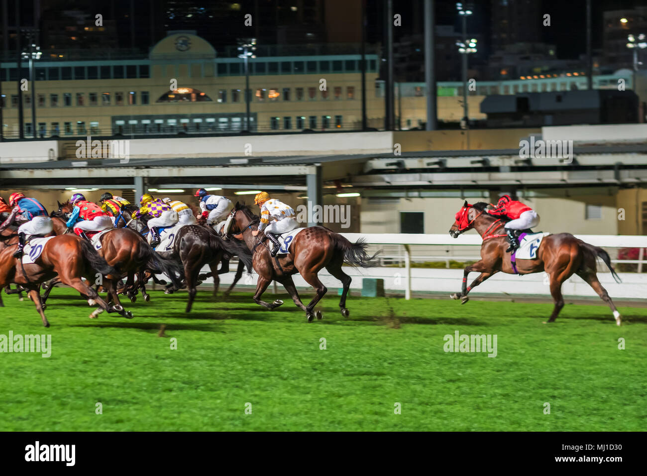 Racehorses ridden by jockeys running fast during the race at racetrack. Striving to victory. Hong Kong Happy Valley race course. Motion blur. Stock Photo