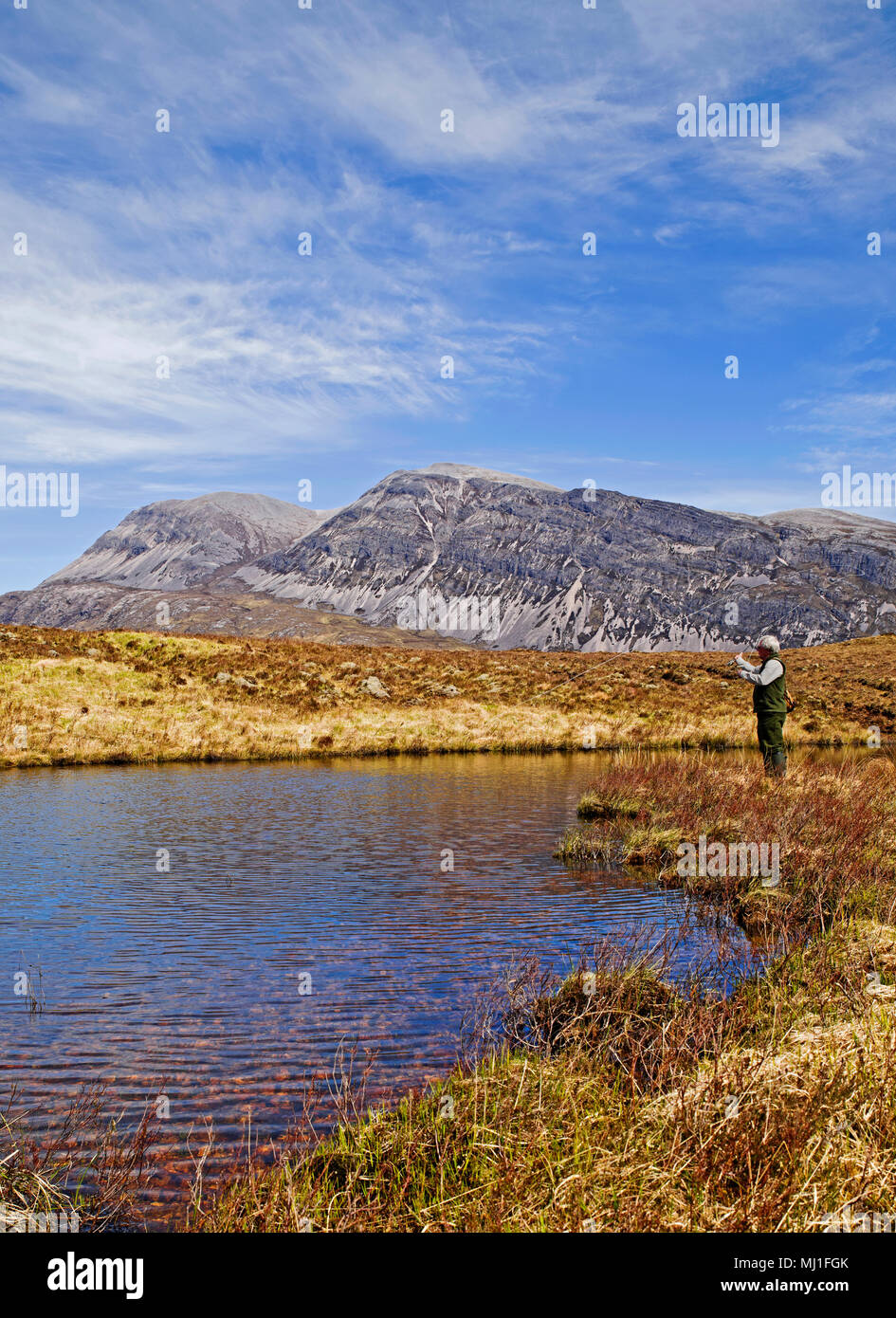 Angler fly-fishing for wild brown trout on hill loch on Reay Forest Estate, mountain Arkle in background, Sutherland, Scottish Highlands, Scotland, UK Stock Photo
