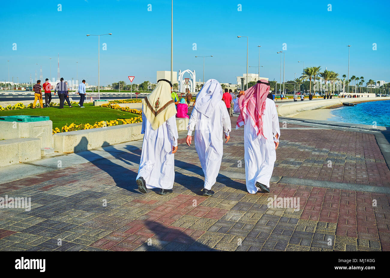 Arabs, dressed in traditional clothes - ghuthrain (headscarf) and dishdasha or thobe (robe) walk along the Corniche promenade, Doha, Qatar. Stock Photo