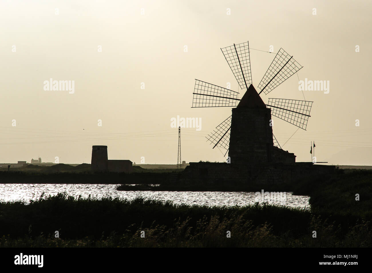 Silhouette of windmill used in salines during the sunset. Photo with high contrast due to backlit sunset situation emphasising the shape of the tradit Stock Photo