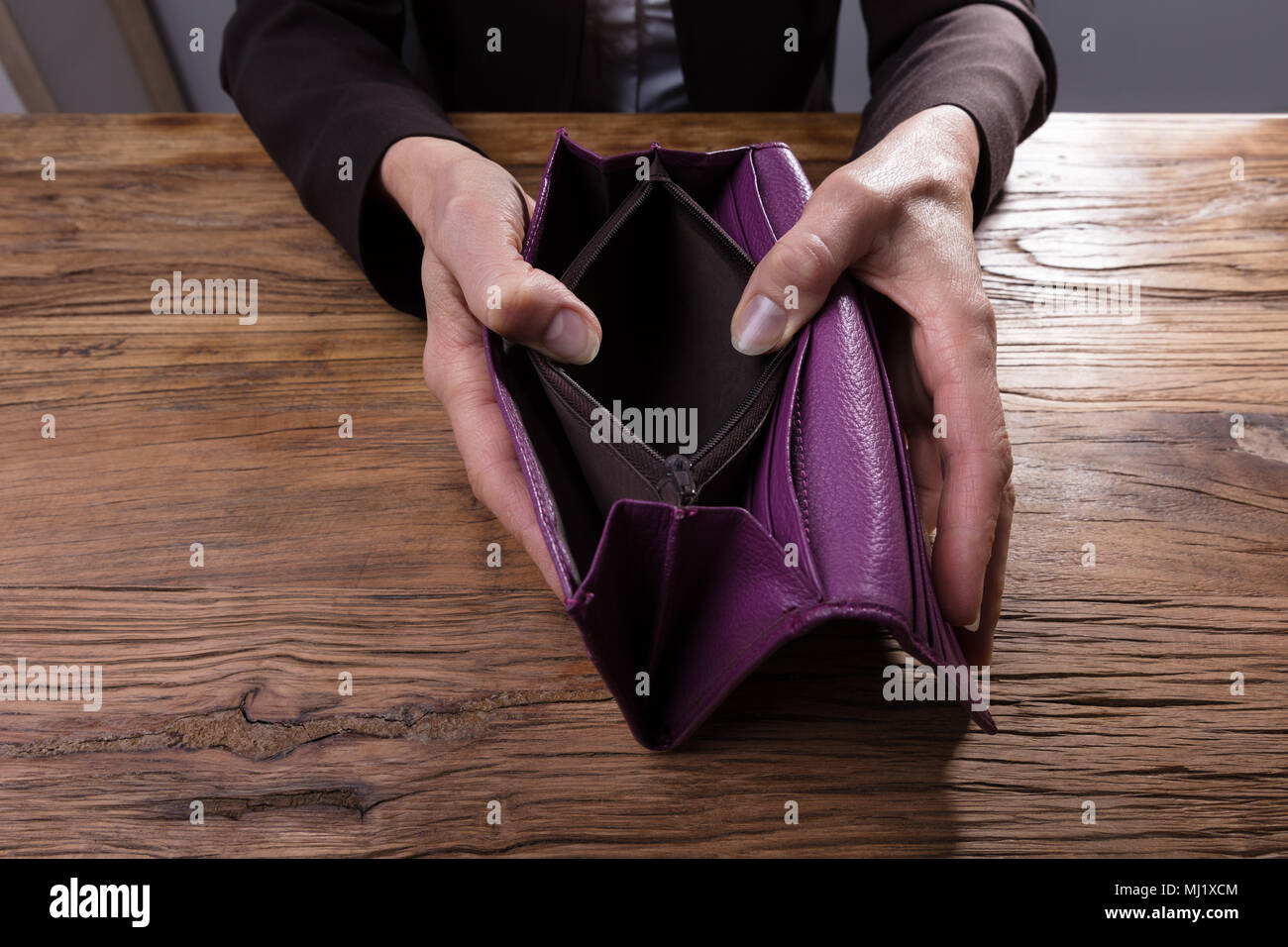 Close-up Of A Businessperson's Hand Holding Empty Purse Over Wooden Desk Stock Photo