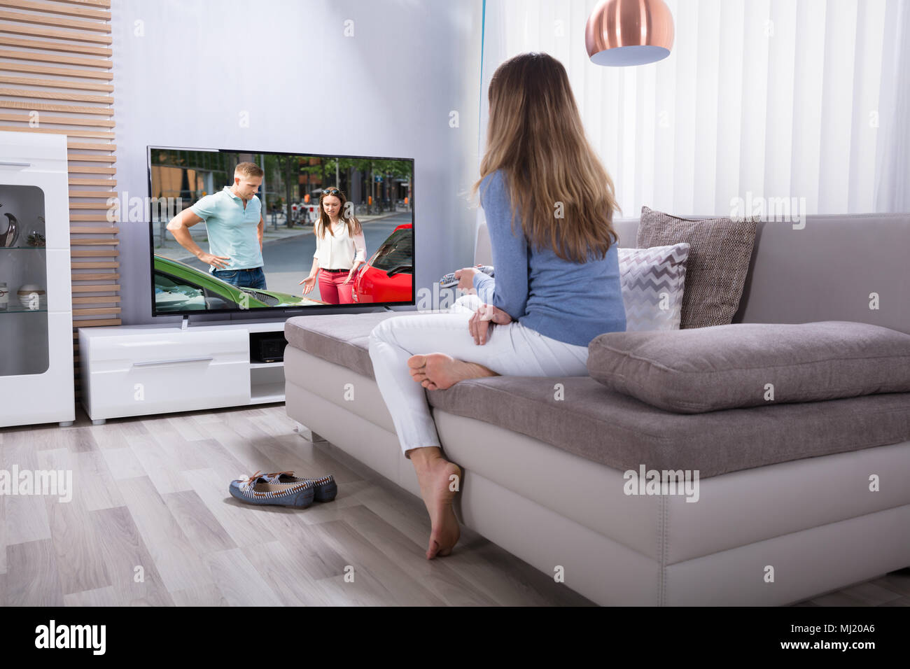 Woman Lying On Sofa Using Calculator While Watching Television At Home  Stock Photo - Alamy