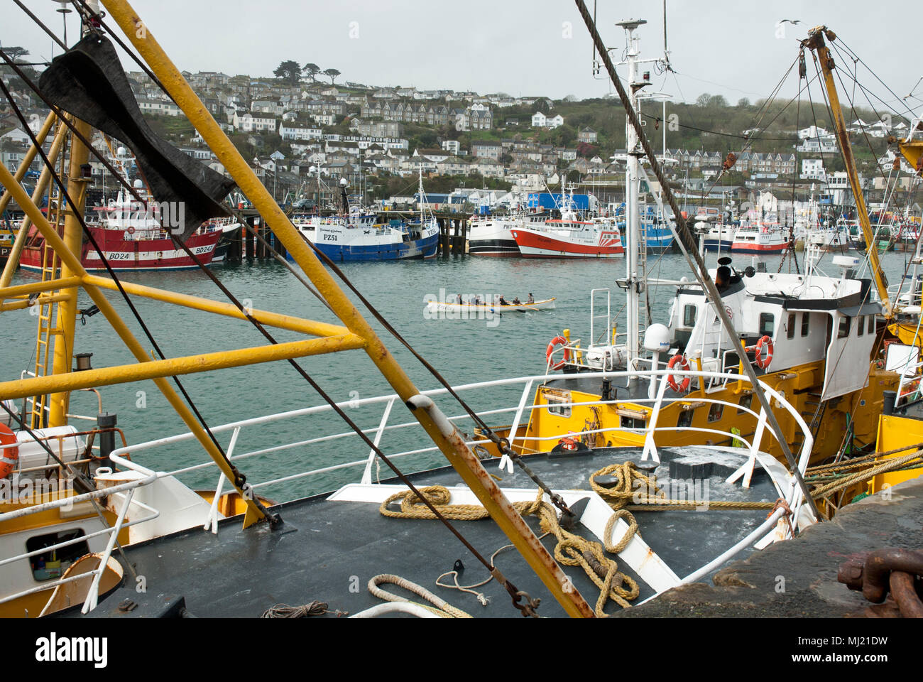 Beam trawlers in the foreground with the traditional gig practicing behind and more colourful fishing boats and Newlyn Town in the background. Stock Photo