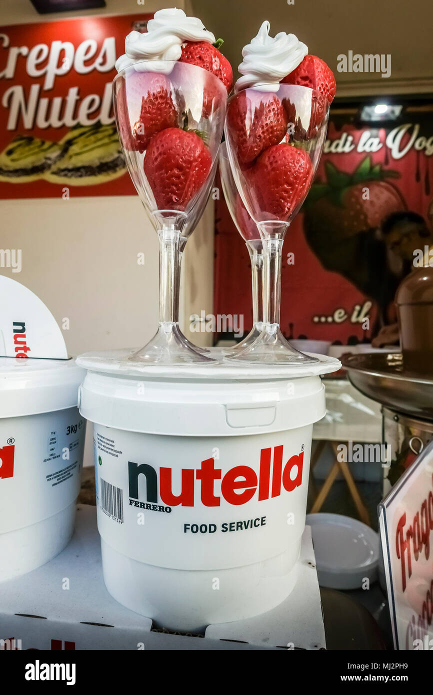 Fresh strawberries with whipped cream in two glasses, on Nutella chocolate jars on display at a kiosk stall. Summer season. Stock Photo