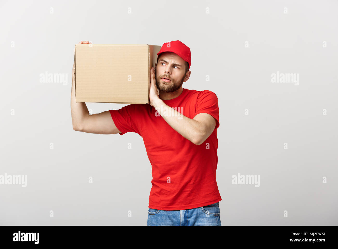 Delivery Concept Portrait Of Curious Caucasian Handsome Delivery Man Listen Inside A Box
