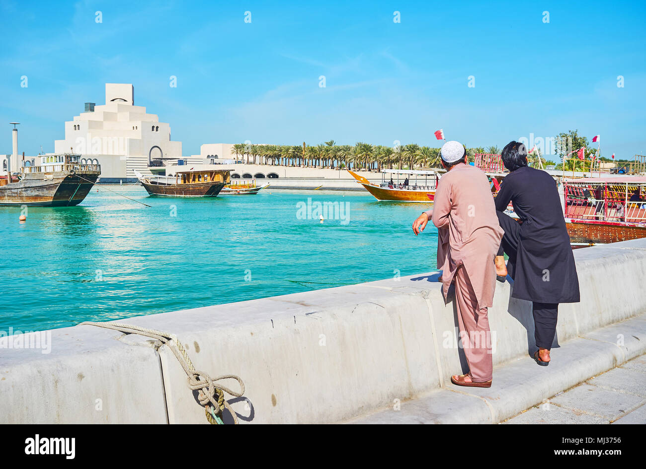 Two Pakistanis in traditional attire watch the seascape and floating dhow boats from Corniche promenade, Doha, Qatar. Stock Photo