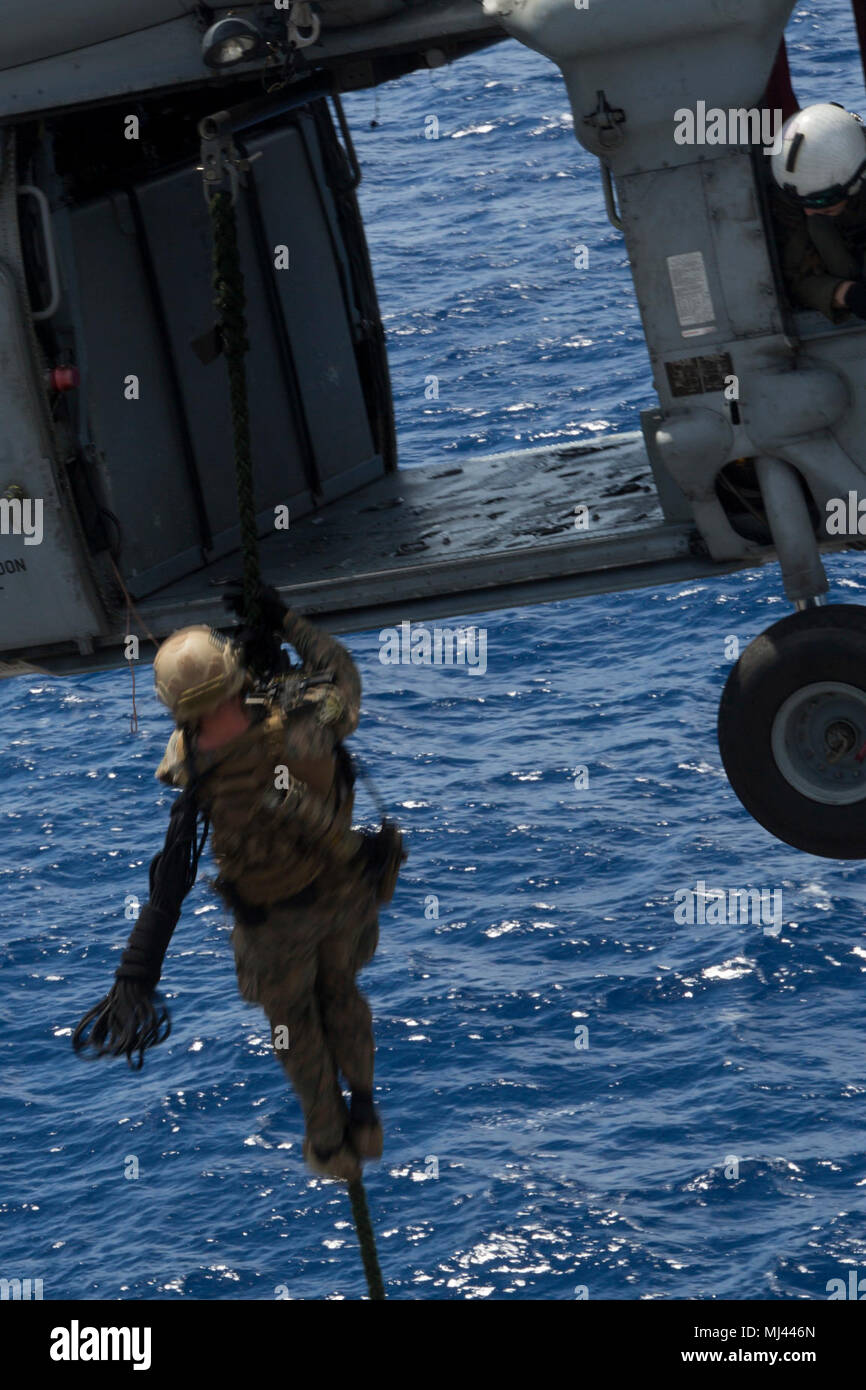 A Force Reconnaissance Marine with Maritime Raid Force, 31st Marine Expeditionary Unit, fast ropes out of an MH-60S Sea Hawk aboard the USS Wasp (LHD-1) while underway in the Pacific Ocean, March 23, 2018. Fast roping allows Marines to enter otherwise inaccessible locations via rope from a hovering aircraft. Marines with Force Reconnaissance Platoon train regularly for quick, tactical raids of targets on both land and sea. As the Marine Corps' only continuously forward-deployed MEU, the 31st MEU provides a flexible force ready to perform a wide range of military operations. (U.S. Marine Corps  Stock Photo